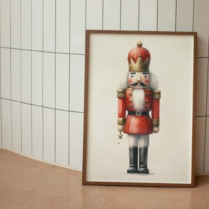 May include: A framed illustration of a traditional nutcracker soldier. The nutcracker is wearing a red and gold uniform with a white beard and a crown. The background is white.