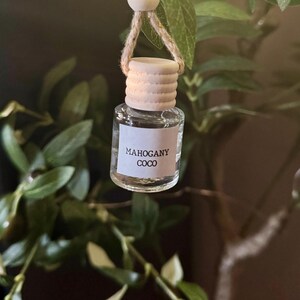 May include: A clear glass bottle with a wooden cap and a string hanging from it. The bottle is labeled "Mahogany Coco".