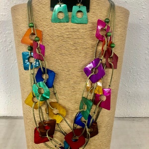 May include: Multi-strand necklace with colorful, iridescent, square-shaped pendants. The necklace is made of gold cord and features green beads. Matching earrings with green iridescent square-shaped pendants.