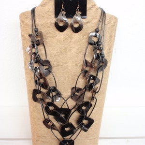May include: A layered black and brown necklace with geometric shapes and matching earrings. The necklace is displayed on a brown stand.
