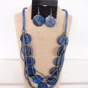 May include: A multi-strand necklace with blue round beads and a matching pair of earrings. The necklace is made of multiple strands of small blue beads with larger blue round beads interspersed throughout. The earrings are simple and feature a single blue round bead.