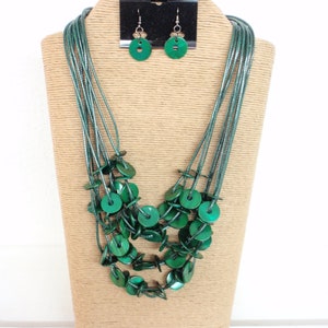 May include: A multi-strand necklace with green round beads and matching earrings. The necklace is made of a dark green cord and the beads are a slightly lighter shade of green.