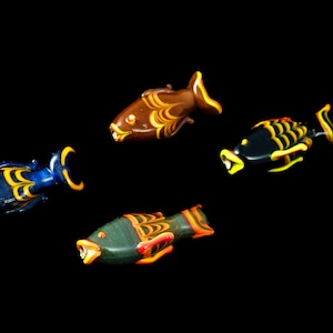 May include: Four glass fish figurines with colorful, swirling patterns. The fish are brown, blue, black, and green with yellow and orange accents.