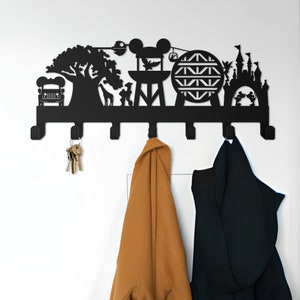 May include: Black metal wall-mounted coat rack with a silhouette design of various Disney theme park attractions, including a tree, a jeep, a castle, a ride, and Mickey Mouse. The rack has six hooks and is hanging on a white wall with two coats hanging on it.