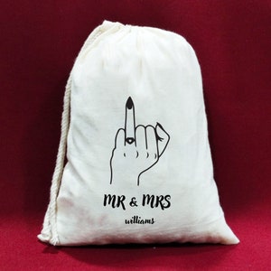 May include: White cotton drawstring bag with a black line drawing of a hand giving the middle finger with a ring on the ring finger. The text "MR & MRS williams" is printed below the drawing.