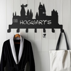 Op de afbeelding: Zwarte metalen wandhaak in de vorm van het kasteel van Zweinstein uit de Harry Potter-serie. De haak heeft zeven haken en de woorden "HOGWARTS" staan op de voorkant.