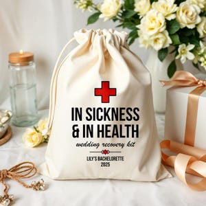 May include: A cream drawstring bag with the text "IN SICKNESS & IN HEALTH" and a red cross symbol. Below the text is "wedding recovery kit" and "LILY'S BACHELORETTE 2025". The bag is on a white surface.