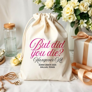 Peut inclure: Un sac en coton crème avec cordon de serrage portant l'inscription "But did you die? Hangover Kit" en rose et noir. Le sac comprend également le texte "KARA'S BACH 2025 DALLAS, TEXAS". Le sac est posé sur une surface blanche.