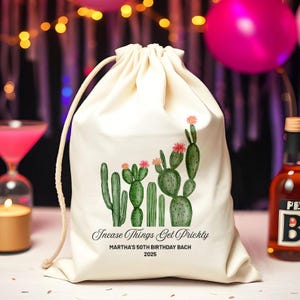 Puede incluir: Una bolsa con cordón de color crema con una ilustración de acuarela de varios cactus con flores rosas. El texto "Incase Things Get Prickly" y "Martha's 50th Birthday Bach 2025" está impreso debajo de los cactus.