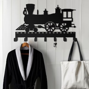 May include: Black metal wall-mounted coat rack shaped like a vintage train engine with six hooks. A black robe hangs on one hook and a white tote bag hangs on another hook.
