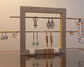 May include: A wooden jewelry stand with four brass rods for hanging earrings and a necklace. The stand has a rectangular frame and is made of light wood. The earrings are a variety of styles and colors, including silver, gold, and green.