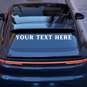 May include: A dark blue car with the text "YOUR TEXT HERE" in white across the rear window. The car has a sleek design with red taillights and a black roof. The image is taken from a slightly elevated angle.