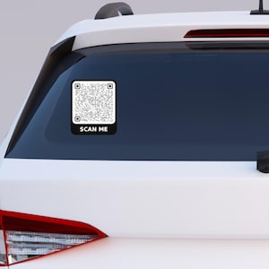 May include: A black and white QR code sticker on the rear window of a white car. The sticker has the text "SCAN ME" in white letters on a black background. The car's taillight is visible.