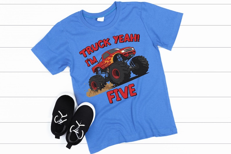 May include: A blue t-shirt with a monster truck graphic and the text "TRUCK YEAH! I'M FIVE" in red. Black and white sneakers are next to the shirt. The shirt features a red monster truck with flames.