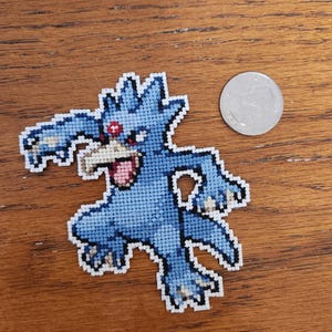 May include: Blue and white cross-stitch of a Pokemon character with red eyes. The character has three arms and is in a fighting pose.