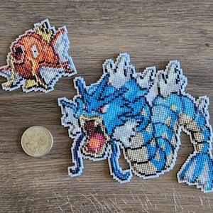 以下が含まれることがあります： ポケモンのキャラクターがクロスステッチで刺繍された2つのパッチ。最初のパッチは青と白のキングドラ、水タイプのポケモン。2番目のパッチは赤とオレンジのギャラドス、水タイプのポケモンです。