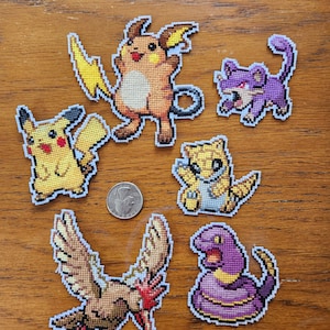 Puede incluir: Seis parches bordados con diferentes personajes de Pokémon. Los personajes incluyen Pikachu, Jolteon, Flareon, Vaporeon, Ekans y Pidgeotto. Los parches están todos sobre una superficie de madera.