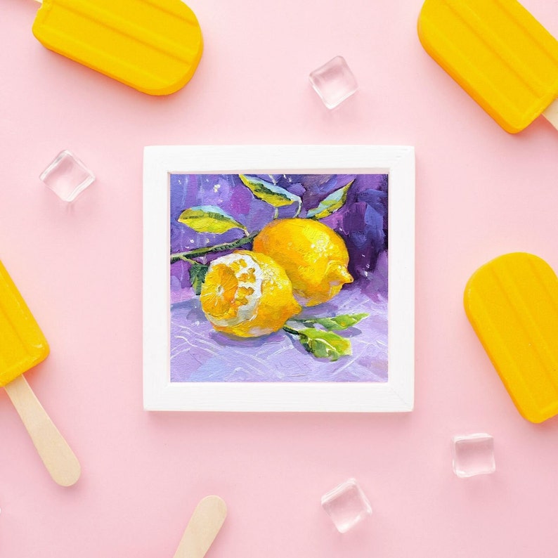May include: A framed painting of two lemons on a purple background. The lemons are yellow and have green leaves. The painting is surrounded by a white frame.