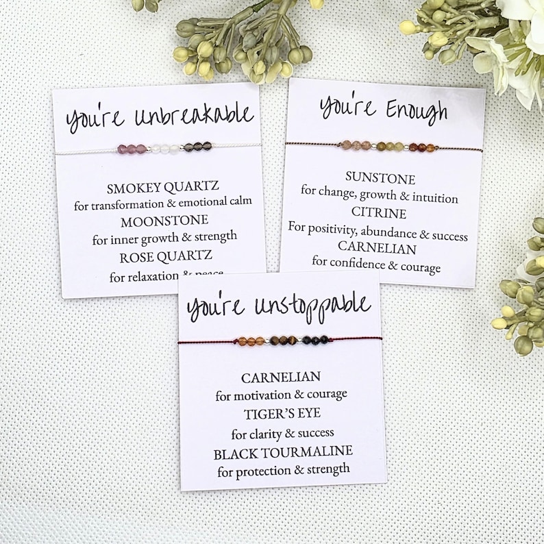 May include: Three cards with the words "you're unbreakable", "you're enough", and "you're unstoppable" printed on them. Each card features a string bracelet with different colored gemstones and a description of the stones' meanings.