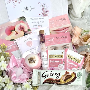 May include: A gift box containing a peach brightening mask, a Pocket Hug card with a heart charm, a glass tube of bath salts, a pink bath bomb, two Twinings Balance tea bags, a Galaxy chocolate bar, and a card with the text With Love.