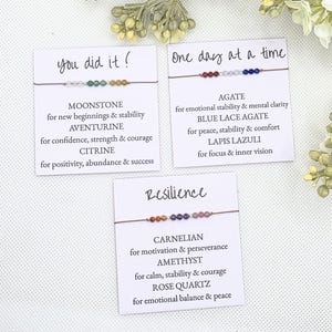 May include: Three cards with beaded bracelets. The cards read "you did it!", "One day at a time", and "Resilience". Each card lists the type of stone and its properties. The bracelets feature moonstone, aventurine, citrine, agate, blue lace agate, lapis lazuli, carnelian, amethyst, and rose quartz.