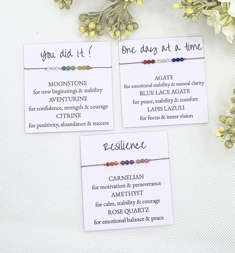 May include: Three cards with inspirational messages and descriptions of the stones used in the bracelets. The bracelets are made with colorful stones and are tied with brown string. The cards read "You did it!" "One day at a time" and "Resilience".