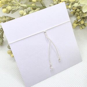 May include: A white string bracelet with silver beads and a silver star charm.