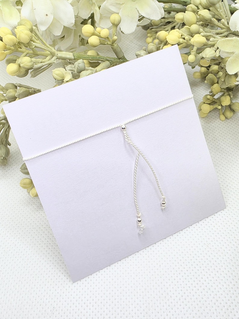 May include: A white string bracelet with silver beads and a silver star charm.
