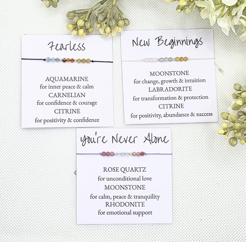 May include: Three cards with the words "Fearless", "New Beginnings", and "You're Never Alone" printed on them. Each card features a bracelet with different colored gemstones and a description of the stones' meanings.