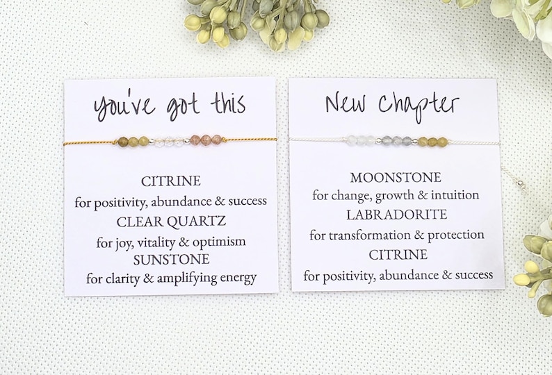 May include: Two cards with the text "you've got this" and "New Chapter" on them. Each card has a bracelet with different colored gemstones and a description of the stones and their meanings.