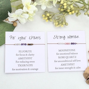 May include: Two cards with text and gemstone bracelets. The first card says "For your exams" and lists the stones: Fluorite, Amethyst, Tiger's Eye. The second card says "Strong woman" and lists the stones: Moonstone, Rose Quartz, Amethyst.