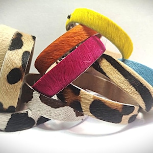 May include: A collection of colorful bracelets with a variety of textures and patterns. The bracelets feature animal print designs, as well as solid colors like yellow, orange, pink, and blue. The bracelets are stacked together.