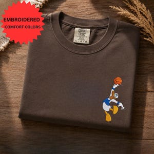 a brown t-shirt with a cartoon character printed on it, placed on a wooden surface.