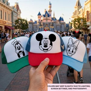 May include: Three character-themed trucker hats with white fronts and mesh backs. The hats feature Mickey Mouse, Goofy, and Daisy Duck designs. The Mickey hat has a red brim, the Goofy hat has a green brim, and the Daisy hat has a light blue brim.