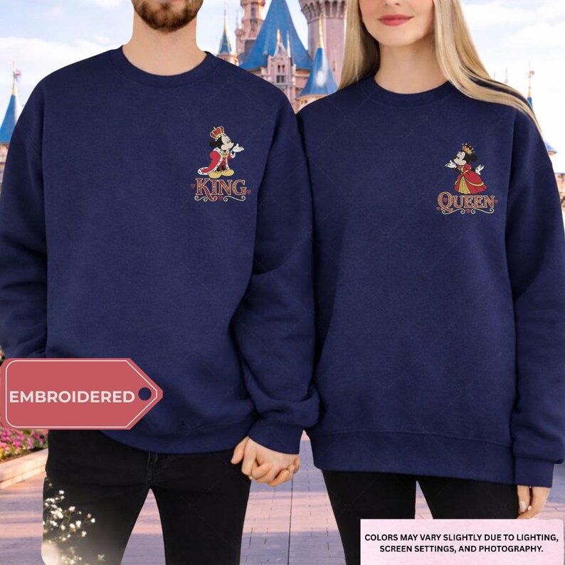 A man and a woman standing together, both wearing matching navy blue sweatshirts with a Disney castle in the background.