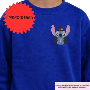 A person wearing a blue sweater with a red starburst and an embroidered character on the front.