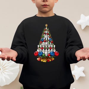 A child wearing a black sweater with a Christmas tree design made of bowling pins and ornaments.