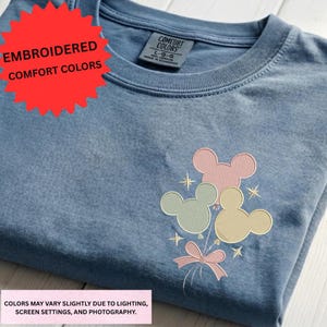 a blue t-shirt with a colorful Mickey Mouse design on the front, including a balloon and stars.