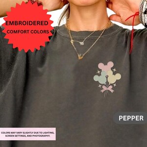 The image is a close-up of a person wearing a gray t-shirt with a Mickey Mouse design and a red ribbon.