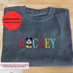 a gray t-shirt with the word "MOCKKEY" embroidered on it, featuring a Mickey Mouse design.
