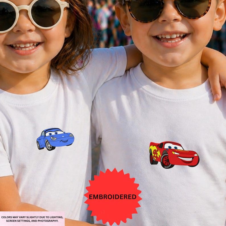 Two children wearing white t-shirts with cartoon car designs on them, smiling and embracing each other.