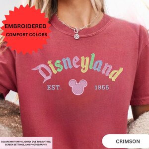 A person wearing a red t-shirt with the text "Disneyland EST. 1955" and a Mickey Mouse logo, along with a necklace.