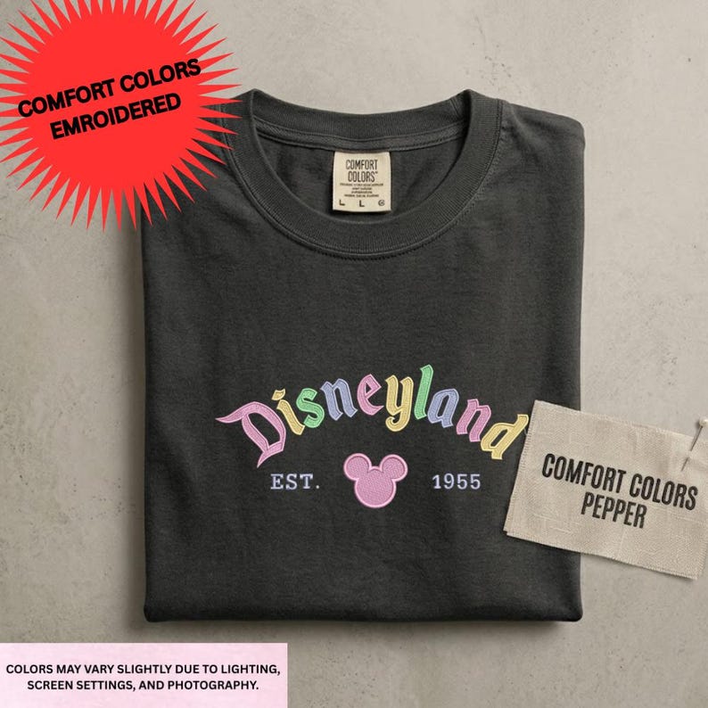a black t-shirt with a Disneyland logo and text, along with a tag that says "Comfort Colors Pepper" and a red starburst that says "COMFORT COLORS EMBROIDED".
