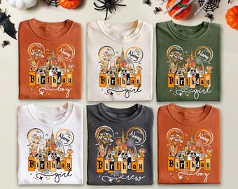 May include: Six folded t-shirts in various colors, including orange, white, and green. Each shirt features a graphic with a castle, Mickey Mouse ears, and the words "Birthday boy", "Birthday girl", or "Birthday crew".