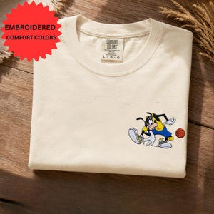 a white t-shirt with a cartoon character printed on it, lying on a wooden surface.