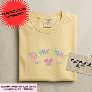 a yellow t-shirt with a Disney logo, a tag indicating the color of the shirt, and a label indicating the comfort colors butter.