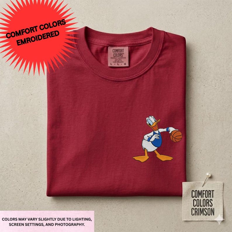 a red t-shirt with a cartoon duck holding a basketball, along with a label indicating that the colors may vary slightly due to lighting, screen settings, and photography.