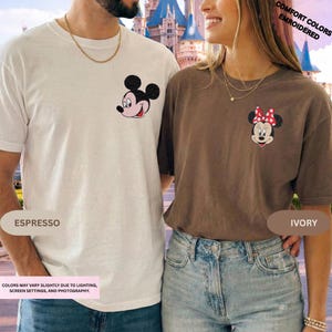 May include: Two t-shirts, one ivory and one espresso, each featuring an embroidered Disney character. The ivory shirt has Minnie Mouse, and the espresso shirt has Mickey Mouse. The text on the image says "Comfort Colors Embroidered".