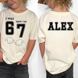 A person wearing a white t-shirt with the text "I WAS 67 NOW I'M ALEX" printed on it.