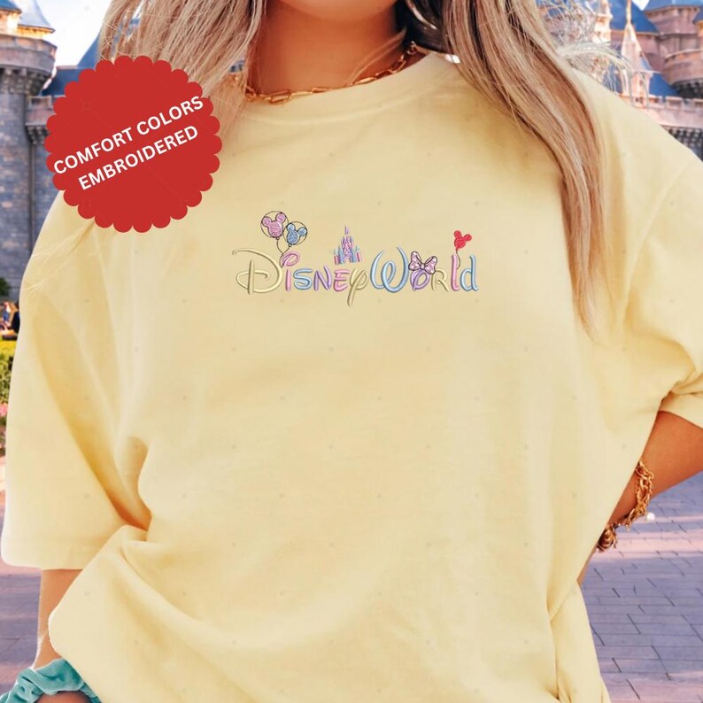 A person wearing a yellow t-shirt with the Disney World logo embroidered on it.